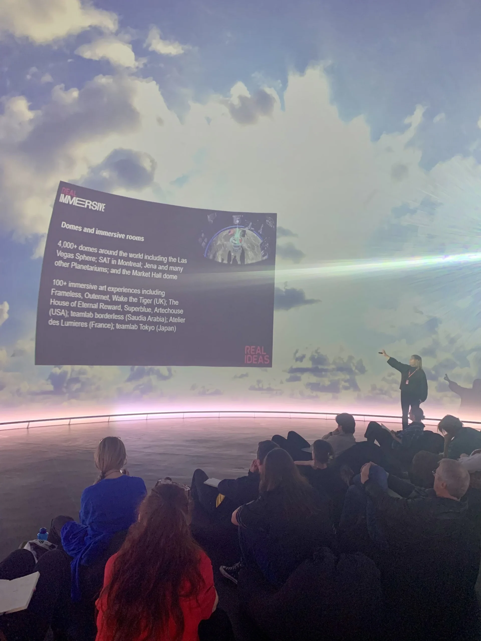 Woman stands in front of large 360 degree screen with an audience
